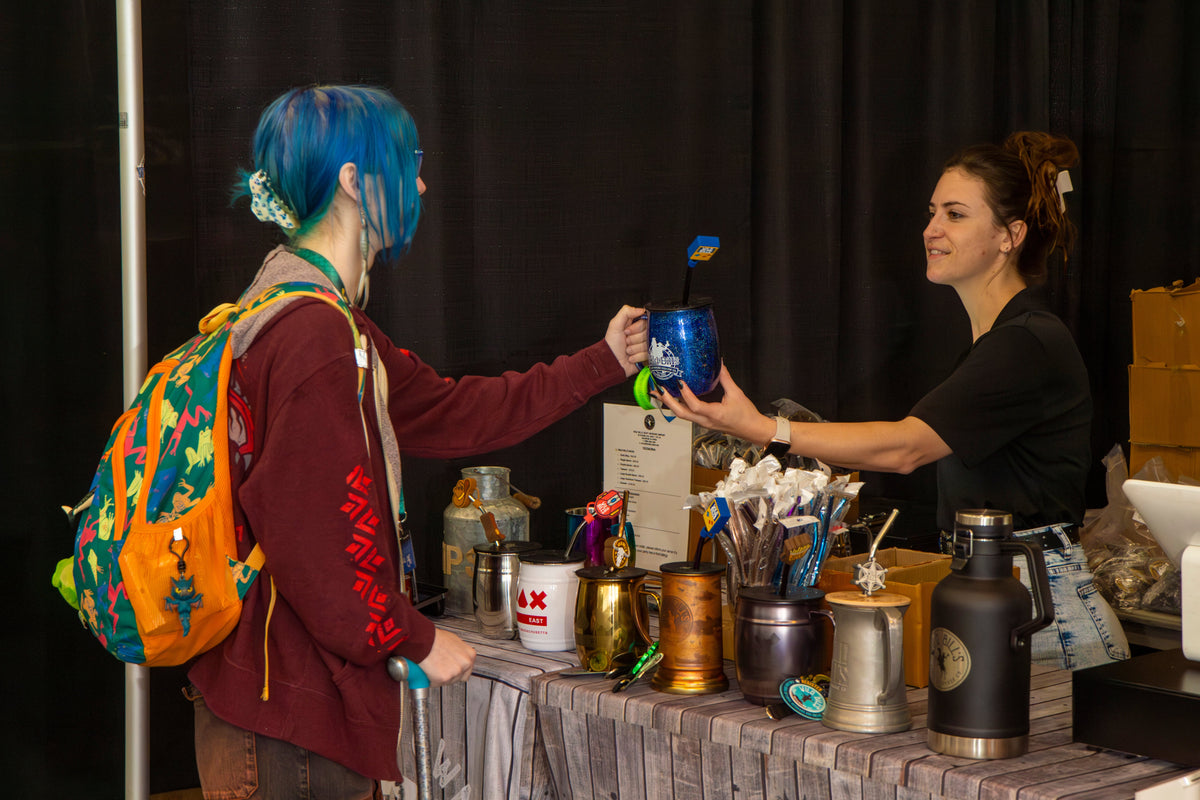 Customer with blue hair receiving a glitter mug at a Wild Bill's booth