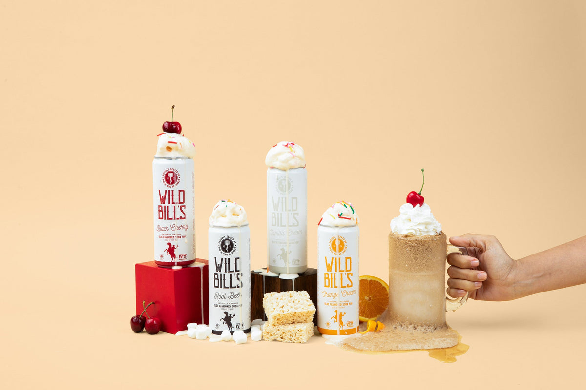 Wild Bill's canned soda lineup with a mug on a beige studio background